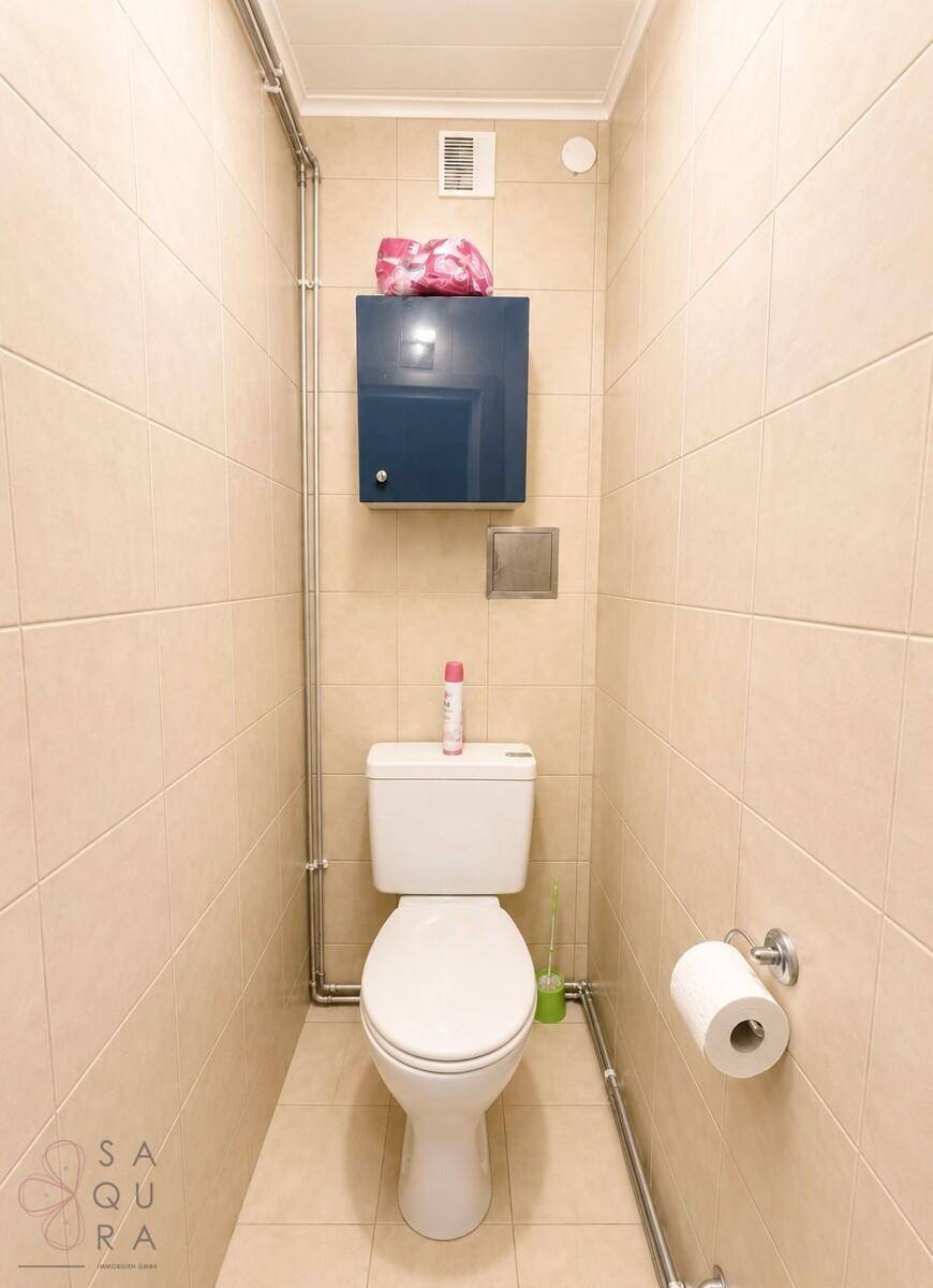 Separates WC mit beigefarbenen Fliesen und Wandregal.