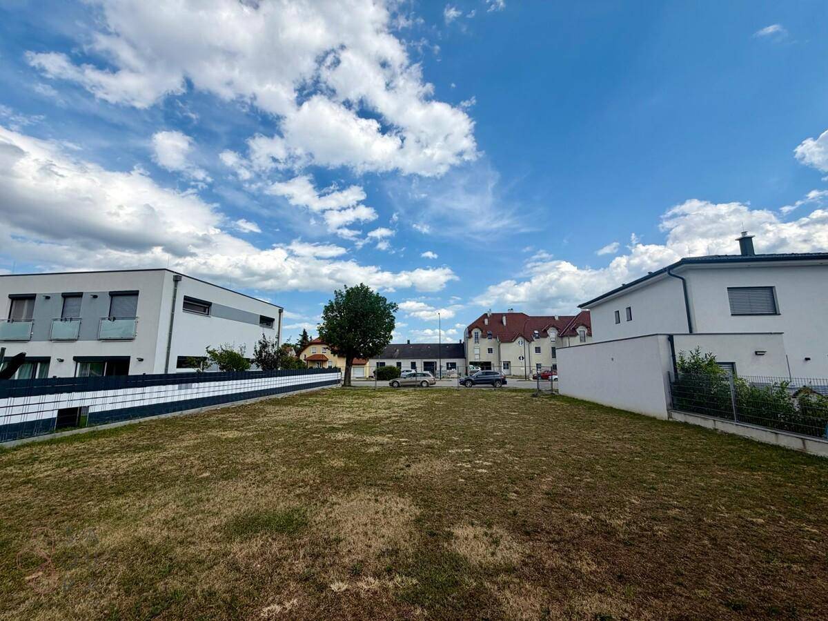 Großes unbebautes Grundstück mit Blick auf die Nachbarschaft und moderne Architektur unter blauem Himmel.
