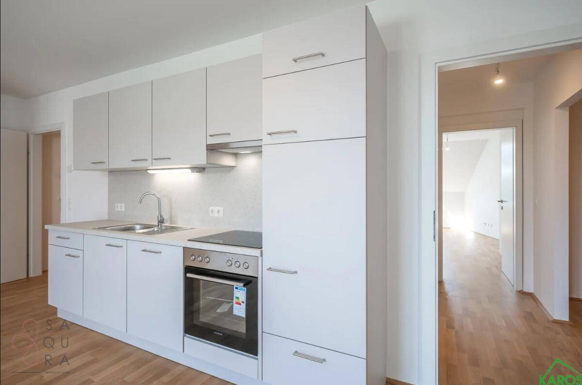 Moderne, helle Küchenzeile mit integriertem Backofen und Kochfeld in einem offenen Wohnbereich.