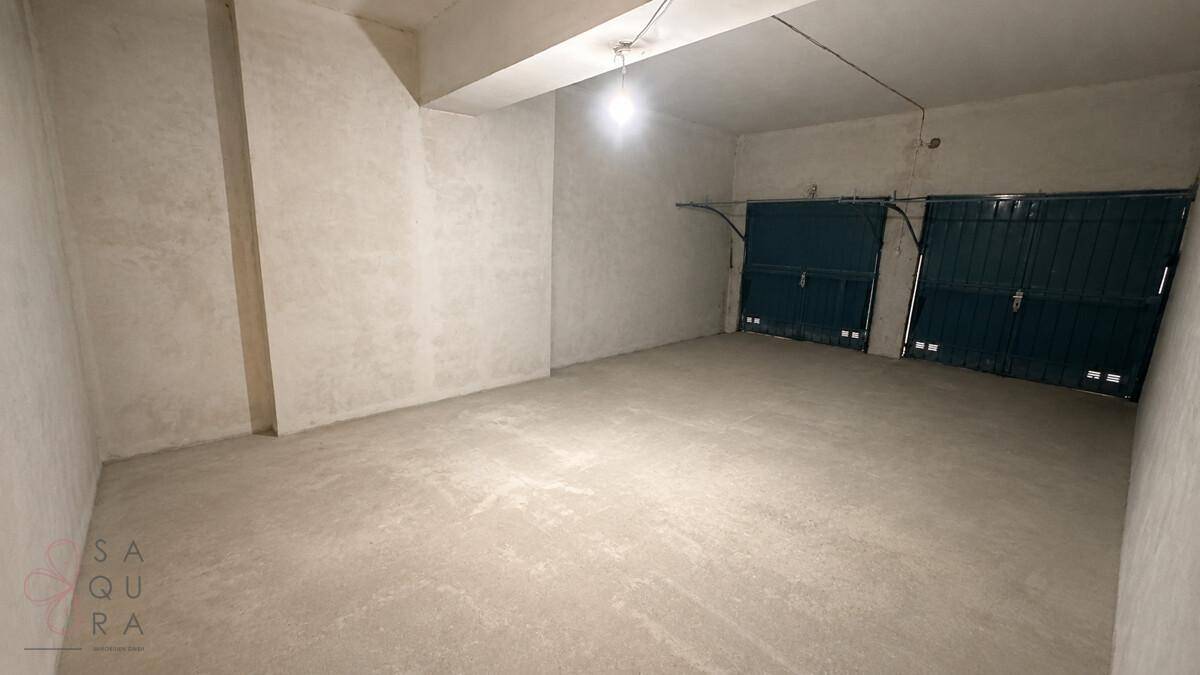 Geräumige leere Garage mit Betonboden und zwei Rolltoren für Fahrzeuge.