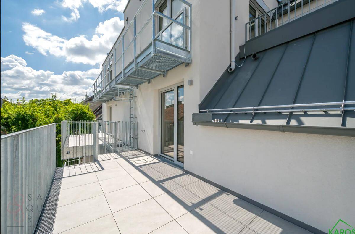 Heller Balkon mit Fliesenboden und moderner Metallkonstruktion, angrenzend an die Gebäudefassade.