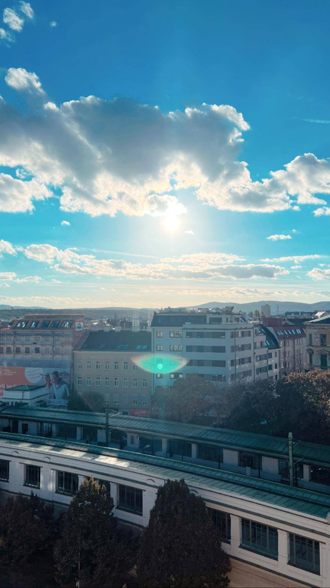Stadtpanorama mit Bahngleisen, Gebäuden und sonnigem Himmel über der Skyline.