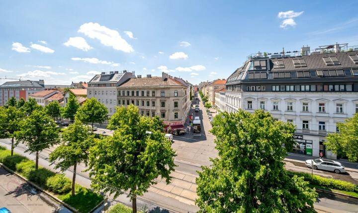 Weitläufiger Blick über eine belebte Stadtstraße mit Bäumen und Gebäuden.