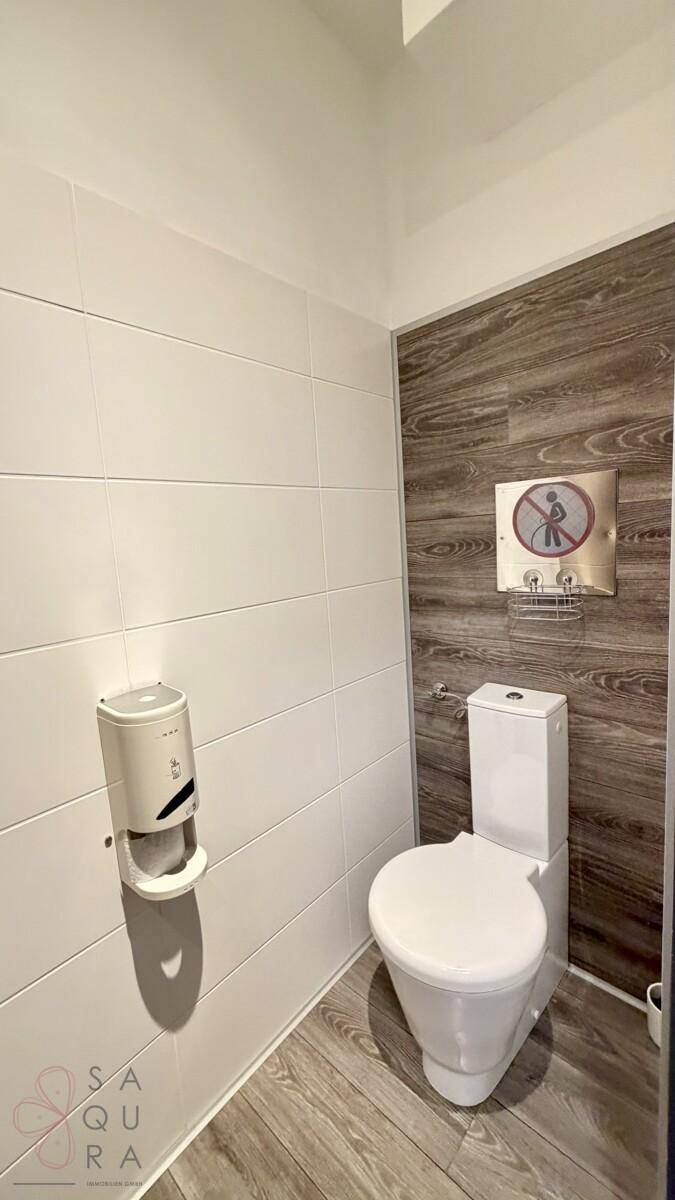 Toilettenraum mit weißen Fliesen, Holzakzentwand und modernem, bodenstehendem WC.