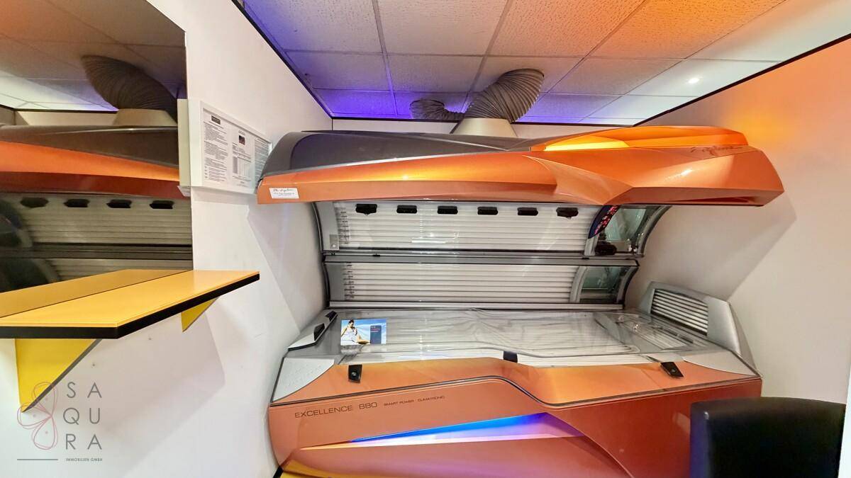 Solariumkabine mit orangefarbenem Bräunungsgerät und heller Innenbeleuchtung in einem funktionalen Raum.