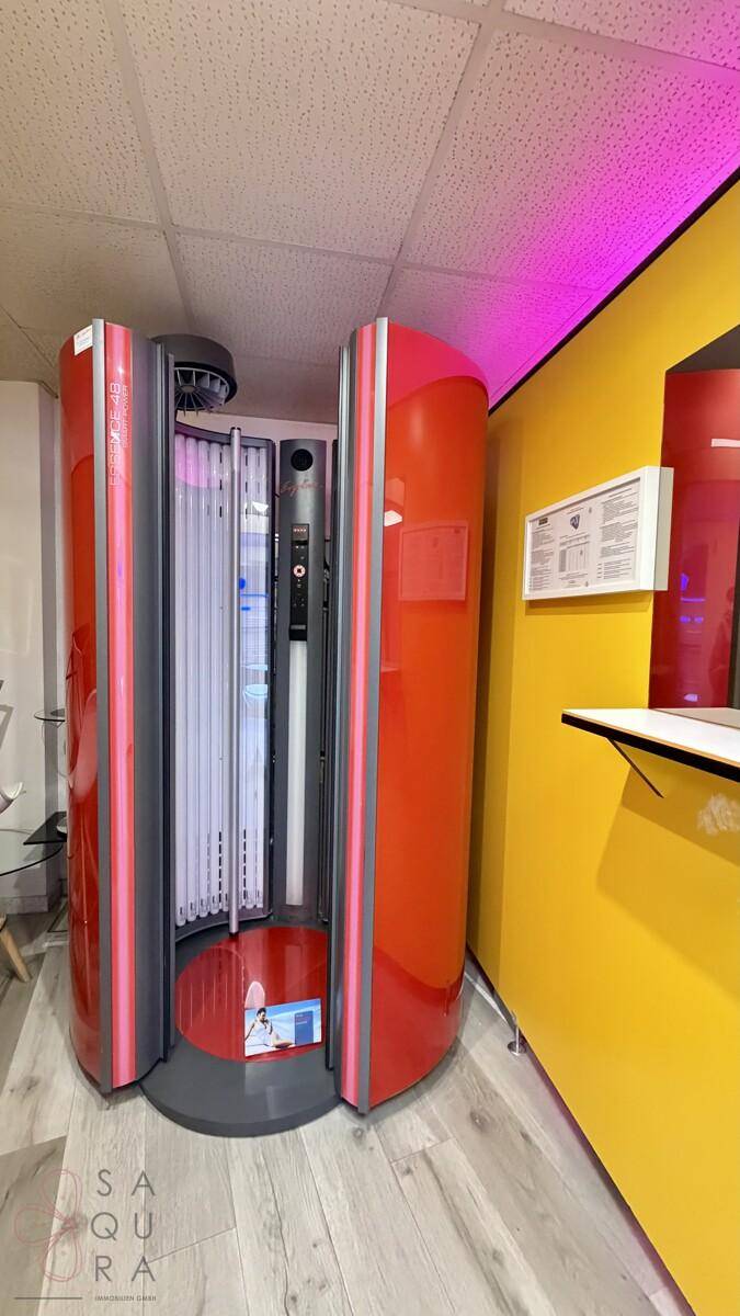 Vertikale Solariumkabine mit leuchtend gelben Wänden und pinkfarbener Beleuchtung für ein besonderes Erlebnis.