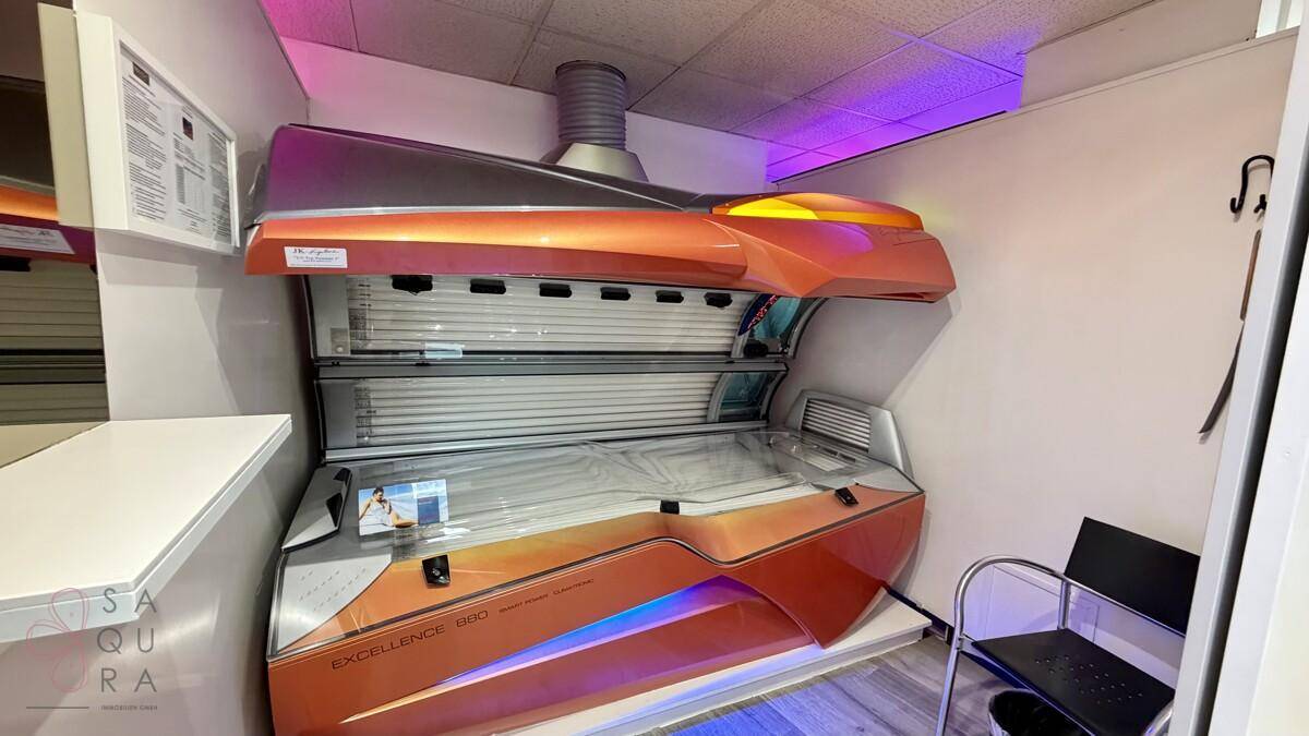 Solariumkabine mit orangefarbenem Bräunungsgerät und heller Innenbeleuchtung in einem funktionalen Raum.