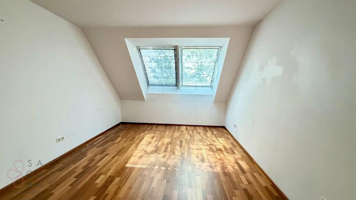 Geräumiges Zimmer mit Holzboden und Dachfenstern, das viel Tageslicht hereinlässt.