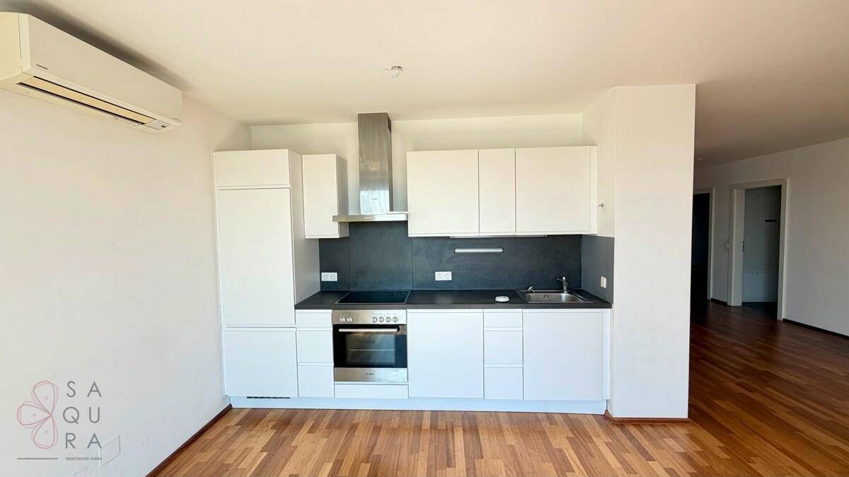 Moderne Küchenzeile mit weißen Schränken, Induktionskochfeld und integrierten Geräten in einem offenen Raum.