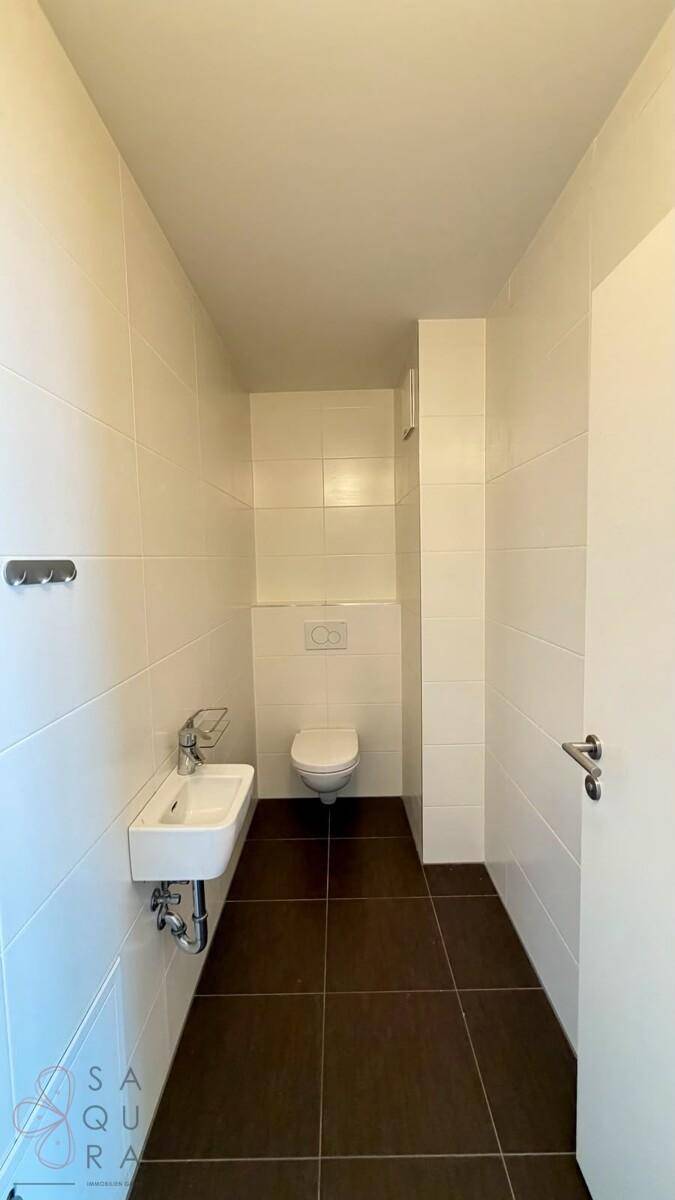 Modernes Gäste-WC mit weißen Fliesen an den Wänden und dunklen Bodenfliesen.