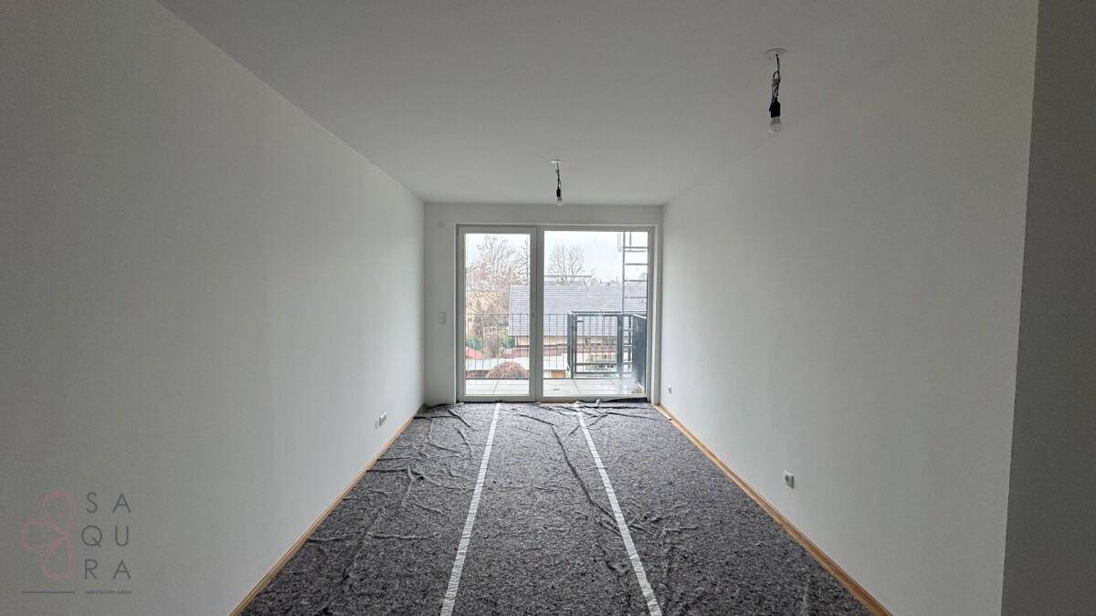 Heller Raum im Rohbau mit Zugang zu einem kleinen Balkon und Blick nach draußen.