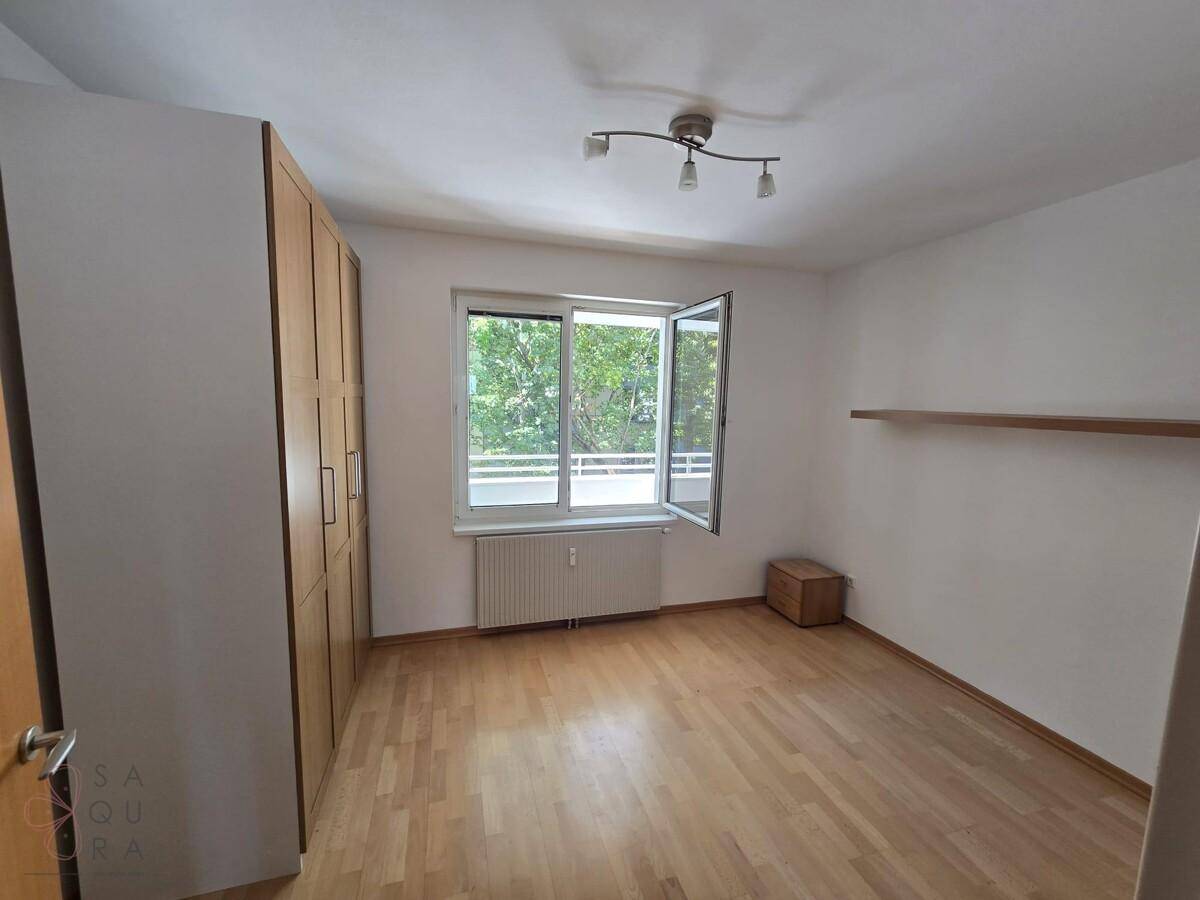 Gemütliches Schlafzimmer mit Holzschrank, Parkettboden und Fenster mit Blick ins Grüne.