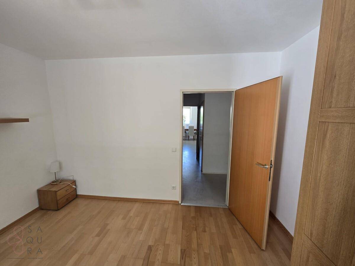 Helles Schlafzimmer mit Parkettboden und Nachttisch, bietet direkten Zugang zu weiteren Räumen.