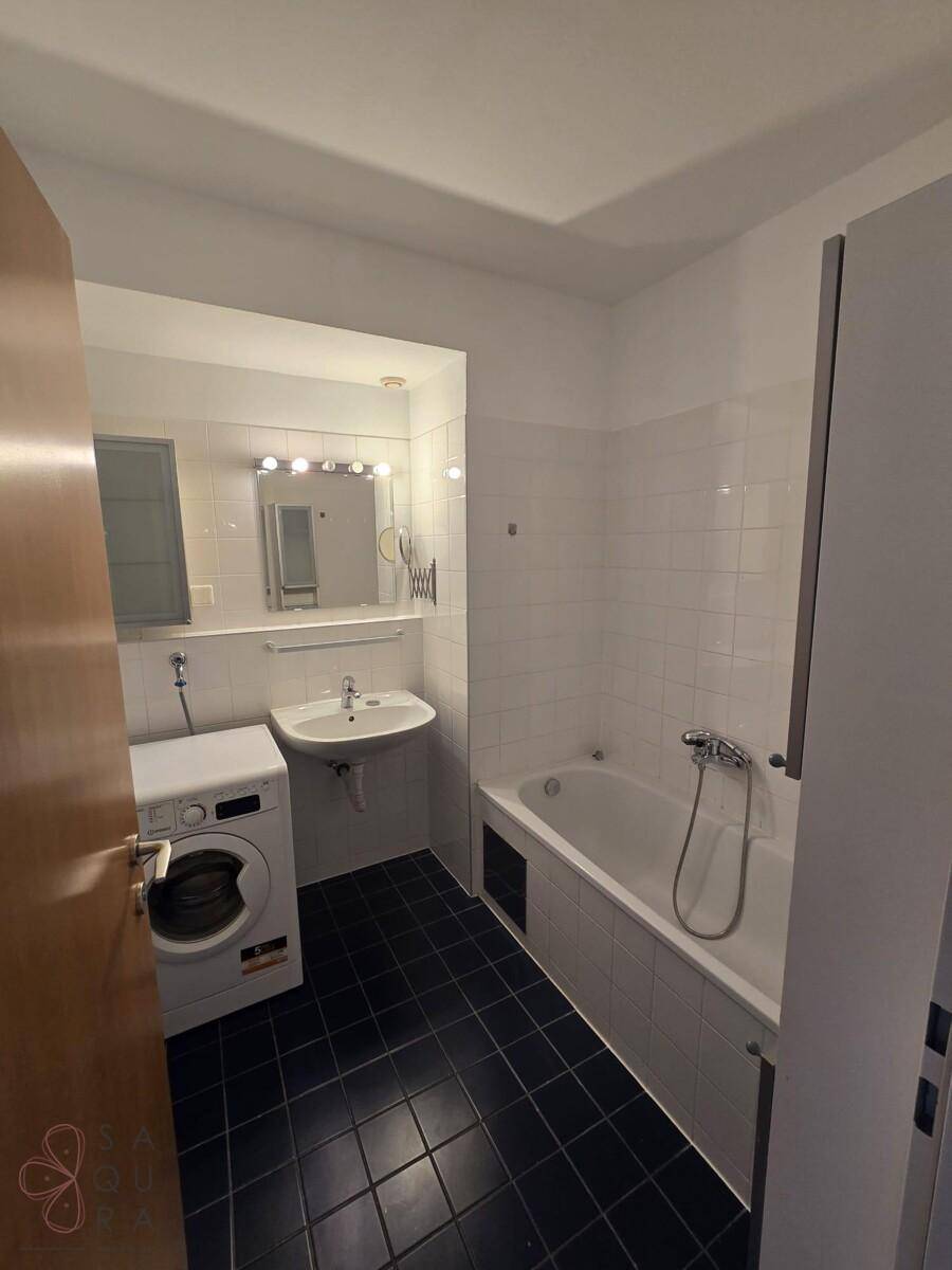 Funktionales Badezimmer mit Badewanne, Waschbecken, Spiegel und integrierter Waschmaschine.