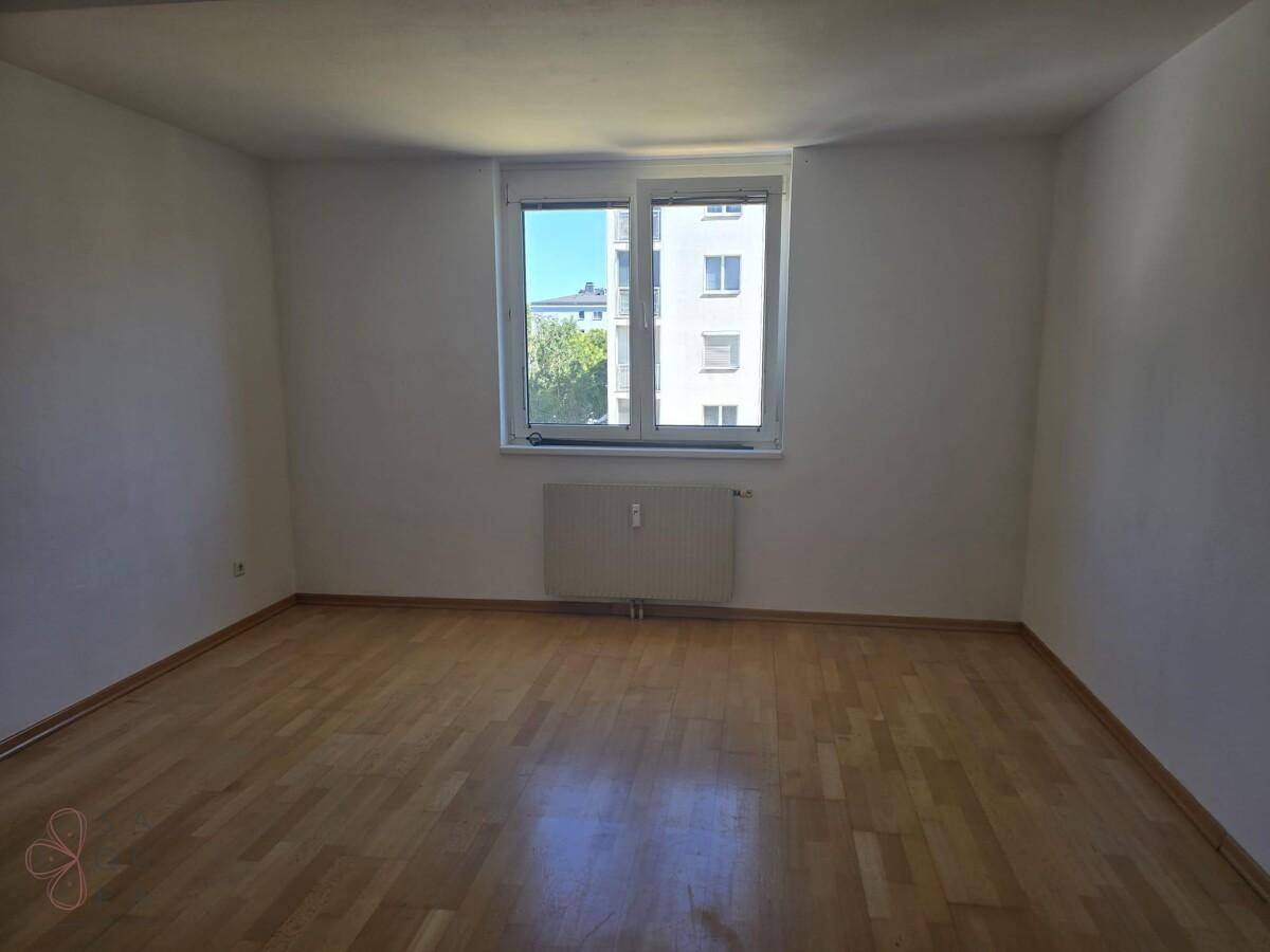 Helles Schlafzimmer mit Parkettboden und großem Fenster, bereit zur individuellen Einrichtung.