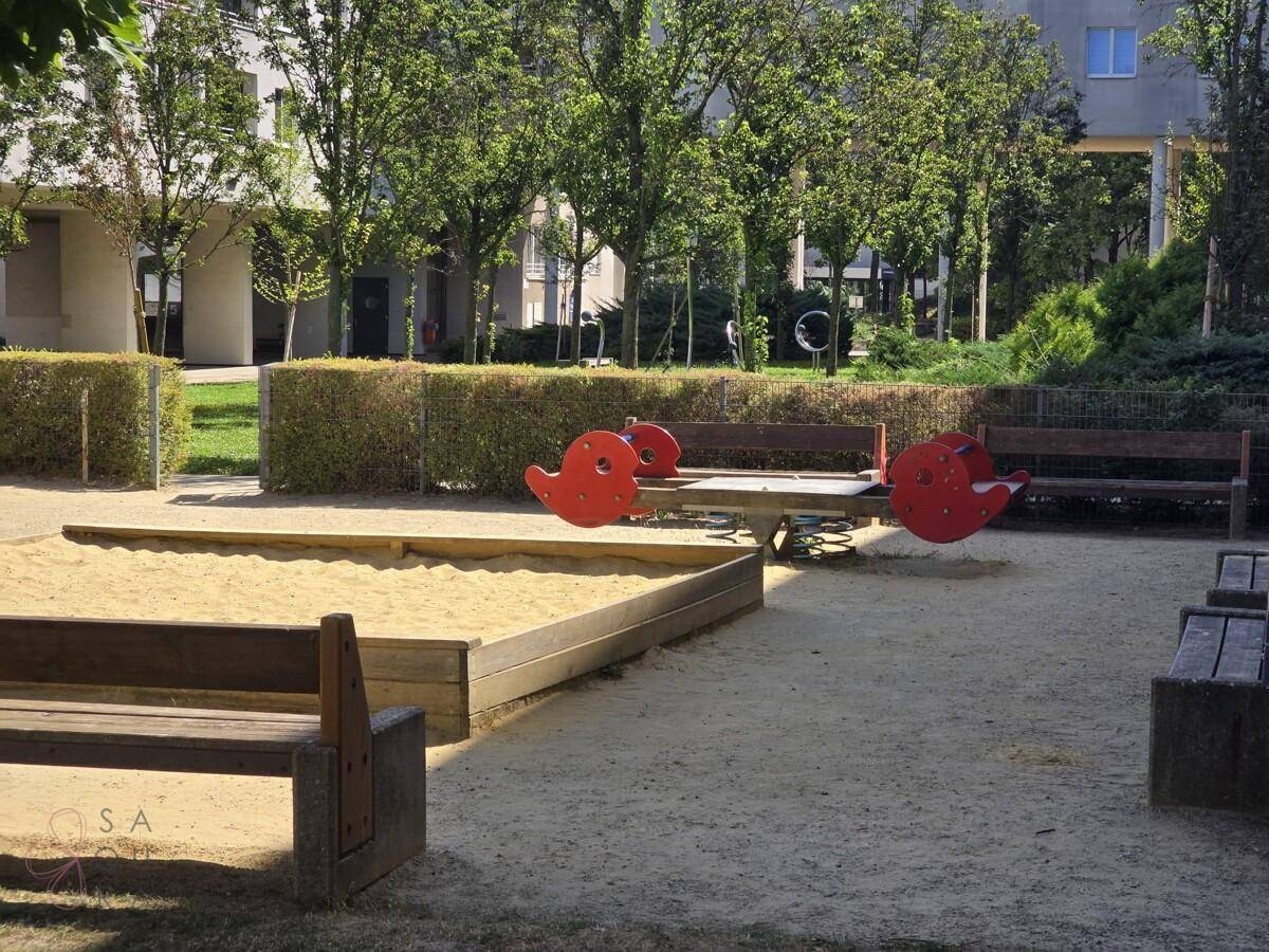 Detailansicht des Spielplatzes mit Sandkasten, Wippe und Sitzbänken im Innenhof.
