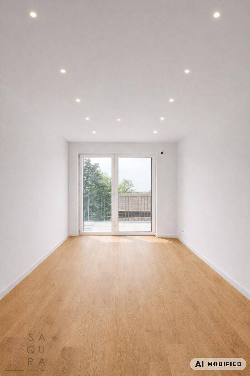 Heller, leerer Raum mit Holzboden und großen Fenstern, die Zugang zu einem Balkon bieten.