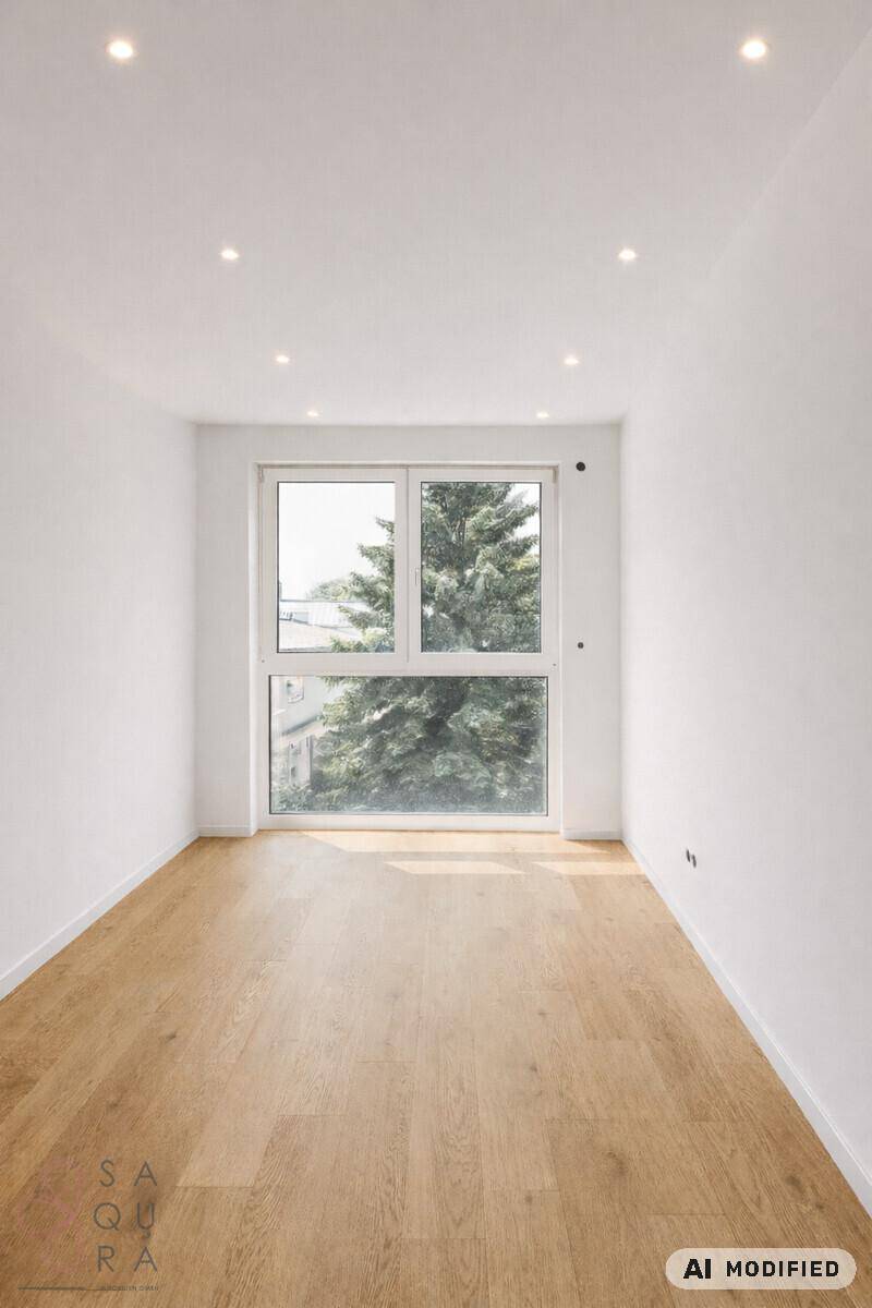 Heller, leerer Raum mit Holzboden und großem Fenster mit Blick ins Grüne.