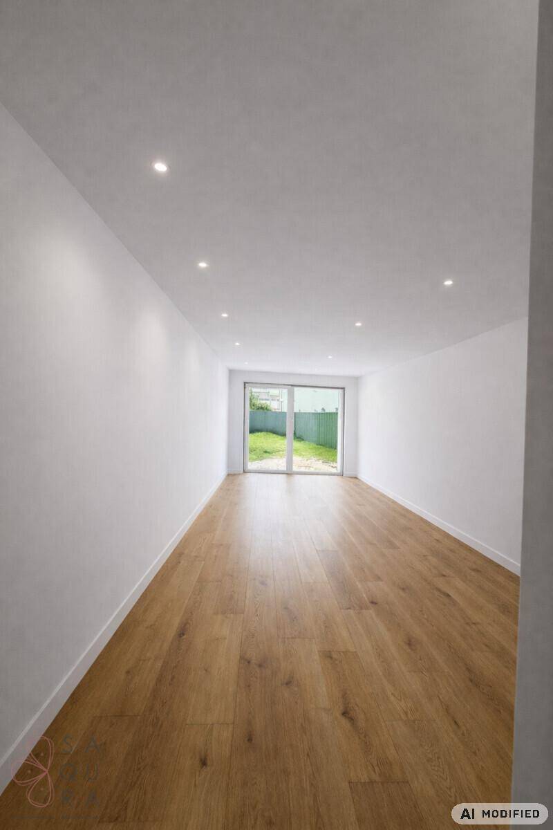 Geräumiger, leerer Raum mit Holzboden und großer Glasschiebetür zum grünen Außenbereich.