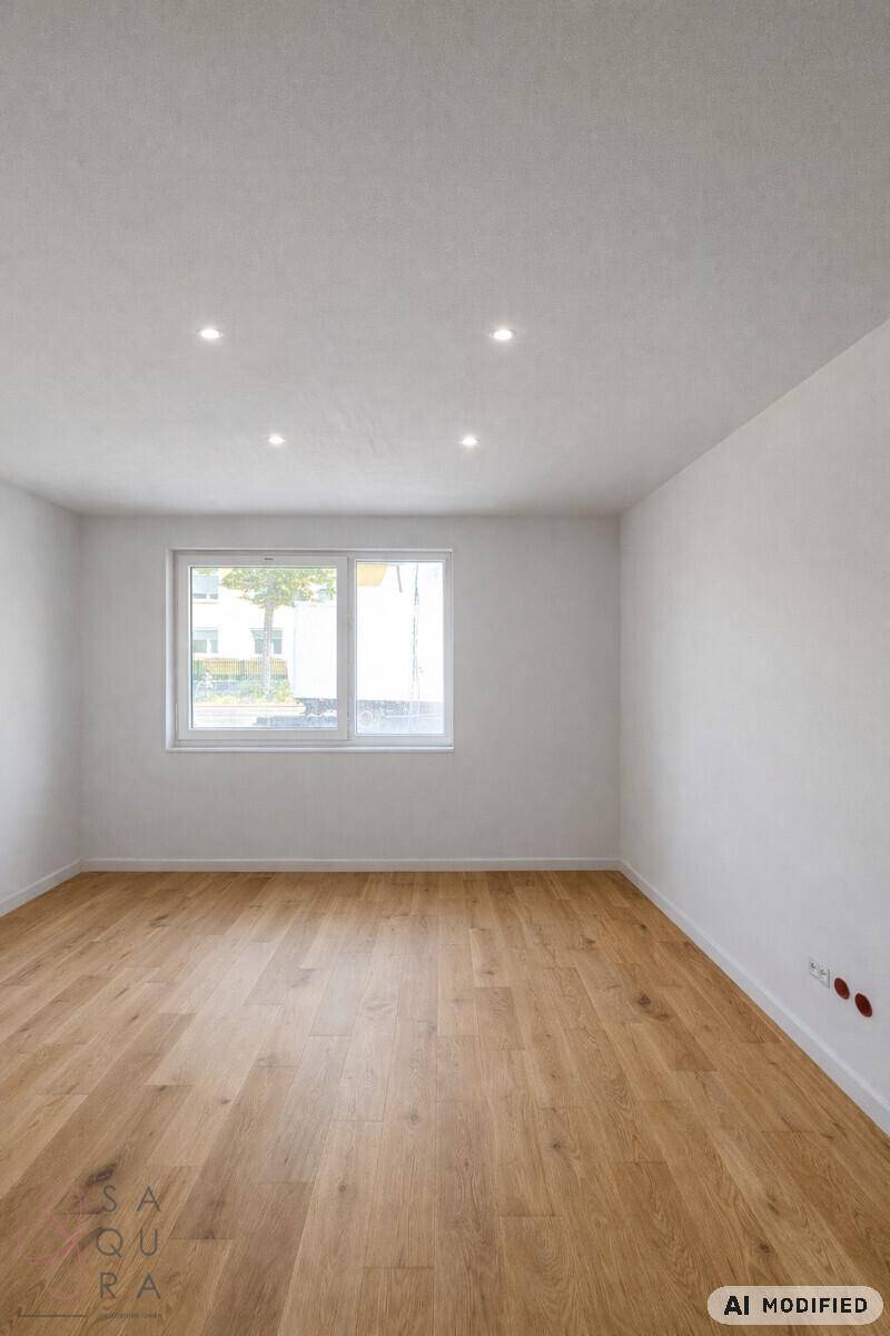 Leeres Zimmer mit Holzboden und einem Fenster, das viel Tageslicht hereinlässt.
