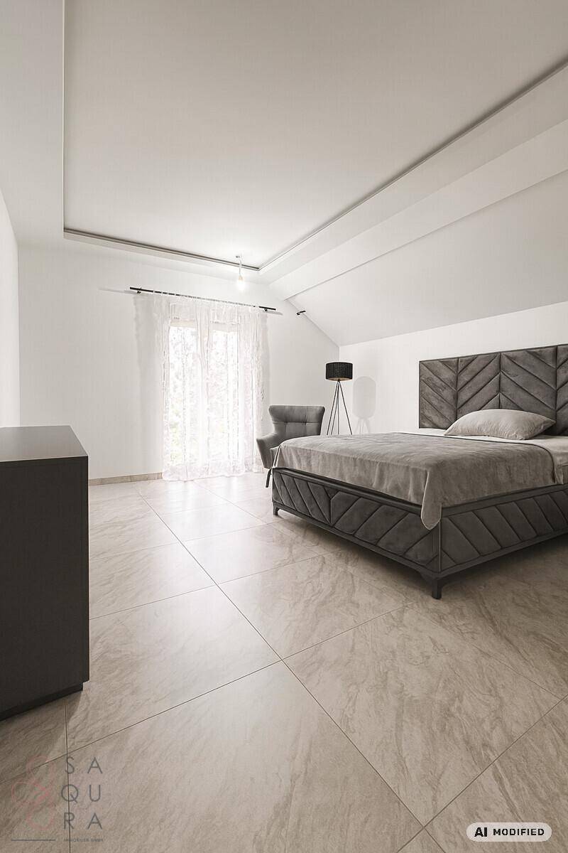 Modernes Schlafzimmer mit grauem Bett, Fliesenboden und schrägen Decken.