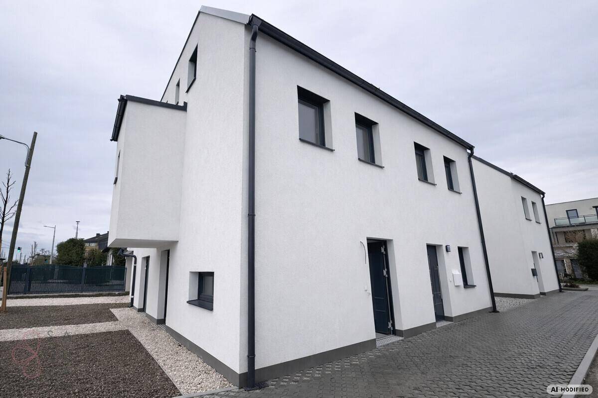 Moderne weiße Fassade eines Neubaus mit dunklen Fenstern und Dach, umgeben von Kiesflächen.