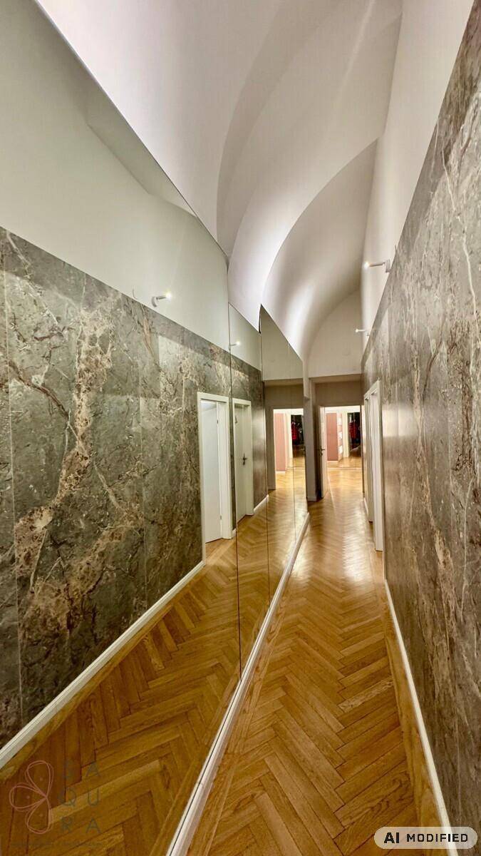 Langer Flur mit Spiegelwänden, Marmorverkleidung und elegantem Fischgrätparkett unter gewölbter Decke.
