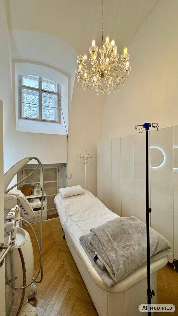 Behandlungszimmer mit Liege, elegantem Kronleuchter und hohem Bogenfenster, auf Fischgrätparkett.