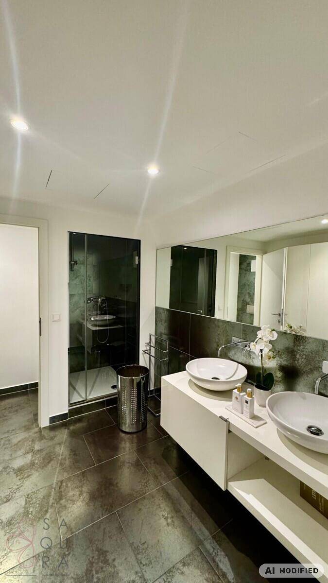 Modernes Badezimmer mit Doppelwaschbecken, großem Spiegel, dunklen Fliesen und einer Glasdusche.