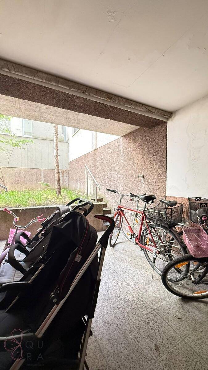 Überdachter Bereich mit Fahrrädern und Kinderwagen, Teil der Wohnanlage.