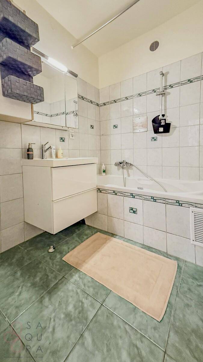 Badezimmer mit Badewanne, Waschbecken und grünen Bodenfliesen, hell und gepflegt.