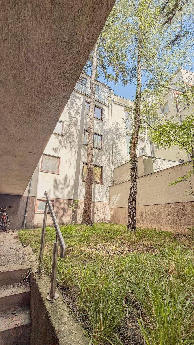 Grüner Außenbereich mit Bäumen und Treppe, Teil der Wohnanlage.