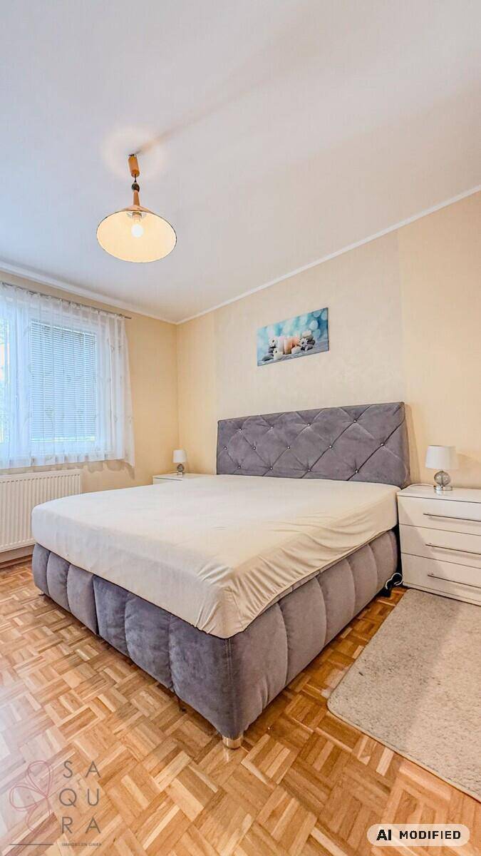 Gemütliches Schlafzimmer mit großem Polsterbett, Parkettboden und Fenster, hell und einladend.