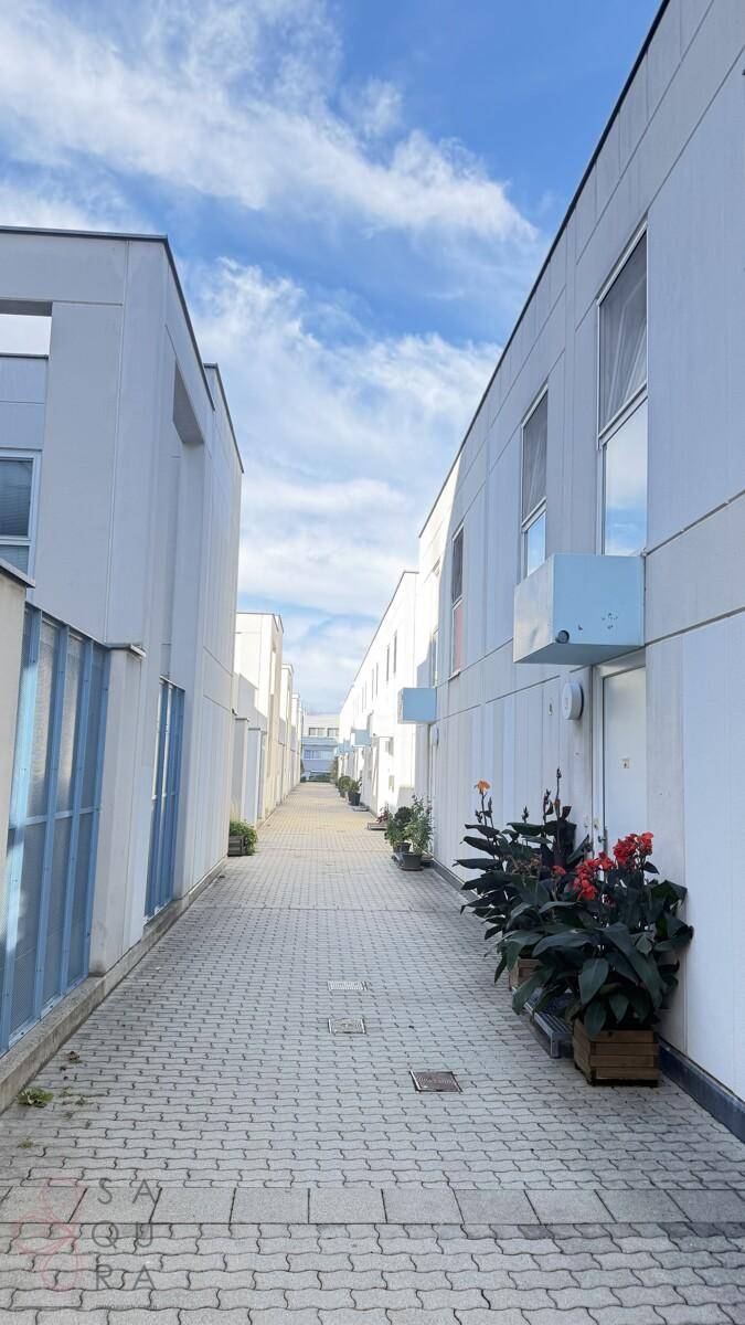 Schmaler gepflasterter Weg zwischen modernen Gebäuden unter blauem Himmel mit einigen Pflanzen.