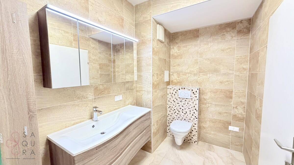 Modernes Badezimmer mit beigefarbenen Fliesen, Waschtisch und wandhängendem WC.