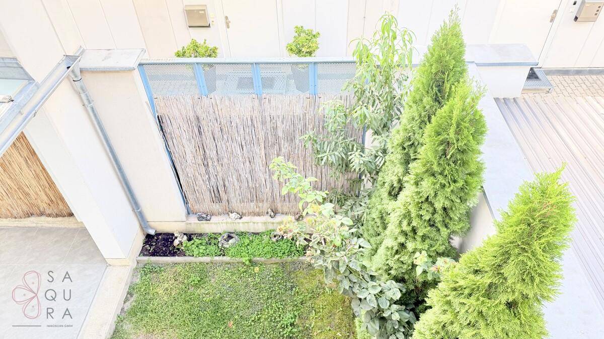 Blick von oben auf einen kleinen Garten mit Rasen, Bäumen und einem Bambuszaun.