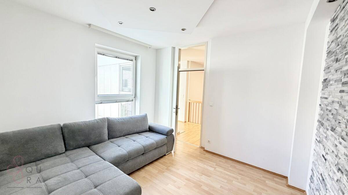 Wohnzimmer mit grauem Sofa, Holzboden und einer dekorativen Steinwand.