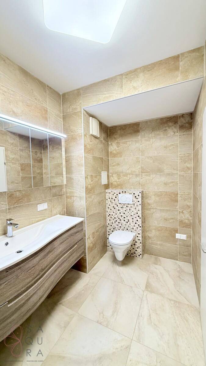 Modernes Badezimmer mit beigefarbenen Fliesen, Waschtisch und wandhängendem WC.