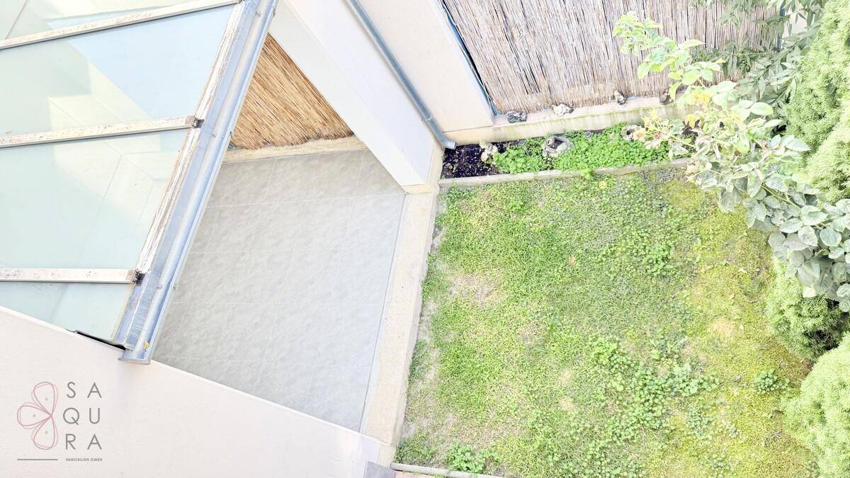 Blick von oben auf einen kleinen, gepflegten Gartenbereich mit Rasen und einer gepflasterten Terrasse.