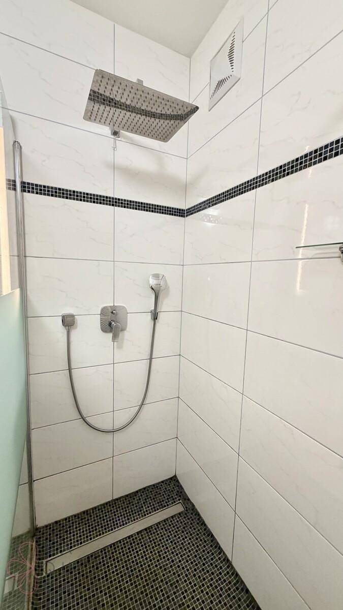 Moderne Dusche mit weißen Fliesen, schwarzem Mosaikband und Regenduschkopf.