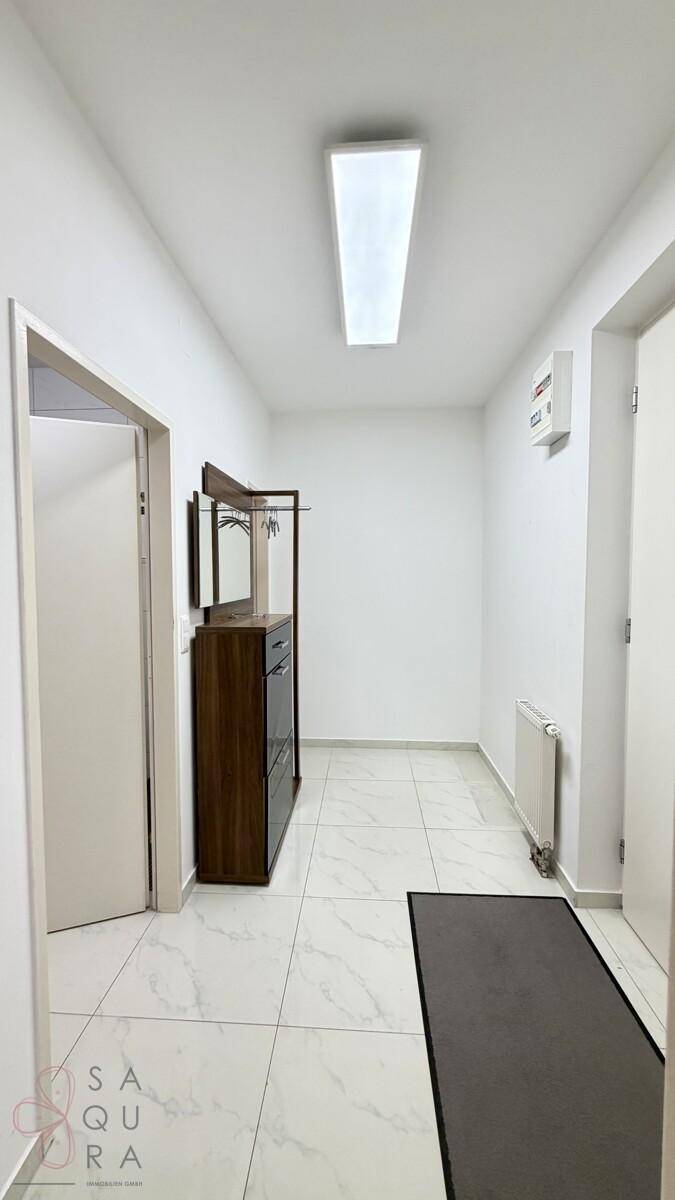 Heller Flur mit weißen Wänden, Fliesenboden und einer modernen Garderobenlösung.