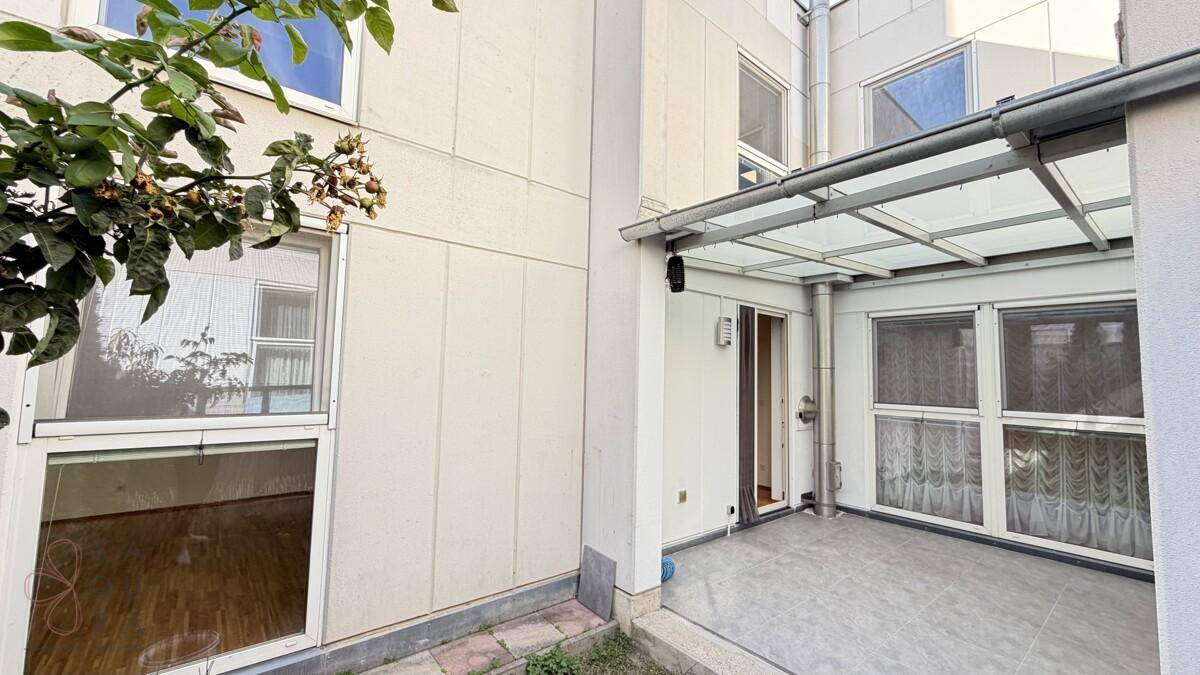 Kleine gepflasterte Terrasse mit Glasüberdachung und Zugang zum Innenbereich des Gebäudes.