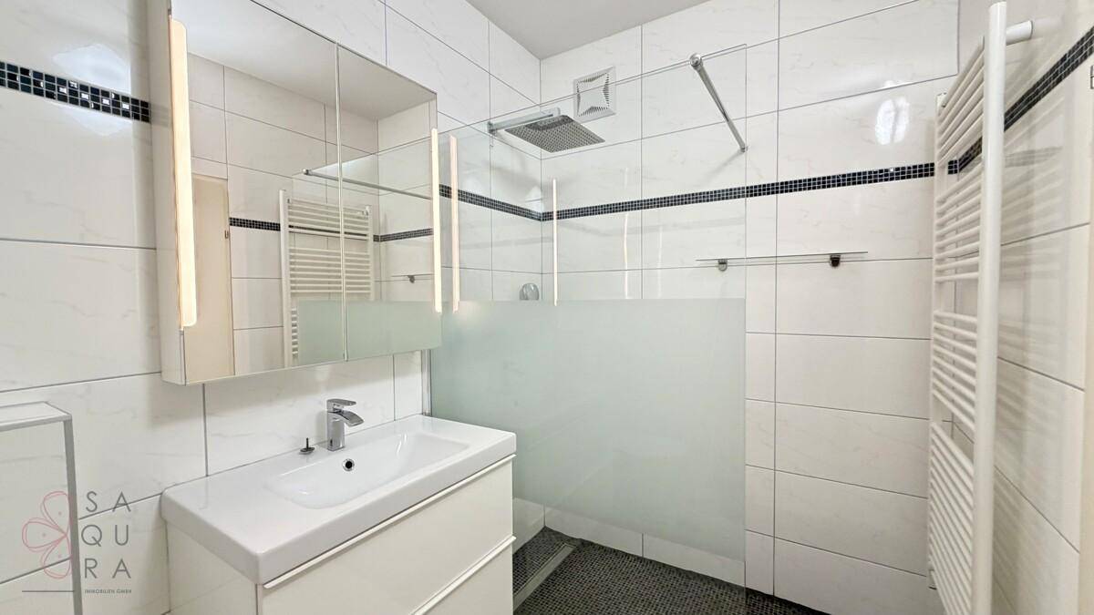 Helles Badezimmer mit moderner Dusche, Waschtischunterschrank und großem Spiegelschrank.