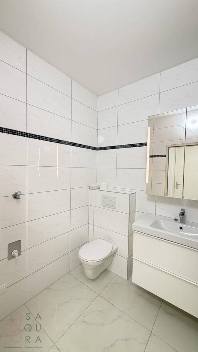 Zeitgemäßes Badezimmer mit Wand-WC, Waschtisch und Spiegelschrank, in hellen Farben gehalten.