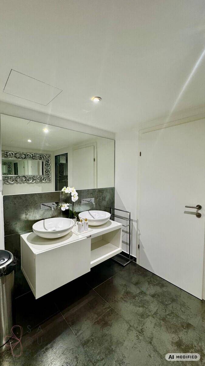 Modernes Badezimmer mit Doppelwaschbecken, großem Spiegel und dunklen Fliesen auf dem Boden.