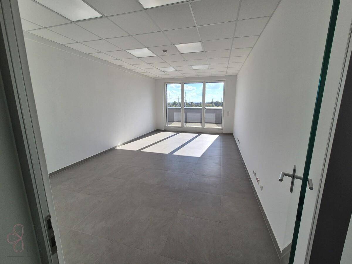 Kleinerer Büroraum mit großen Fenstern, die viel Tageslicht hereinlassen, und modernen grauen Fliesen.