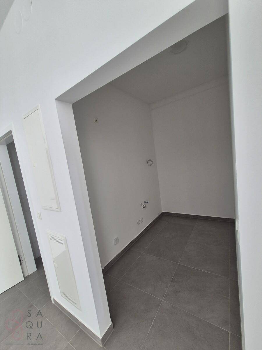 Kleiner Hauswirtschaftsraum mit weißen Wänden und grauen Fliesen, vorbereitet für Anschlüsse.