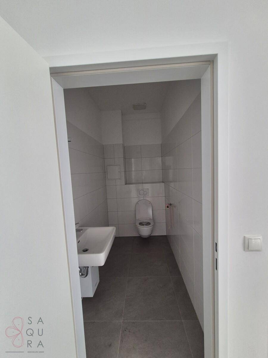 Modernes WC mit weißer Wandfliesenverkleidung, Waschbecken und wandhängender Toilette.