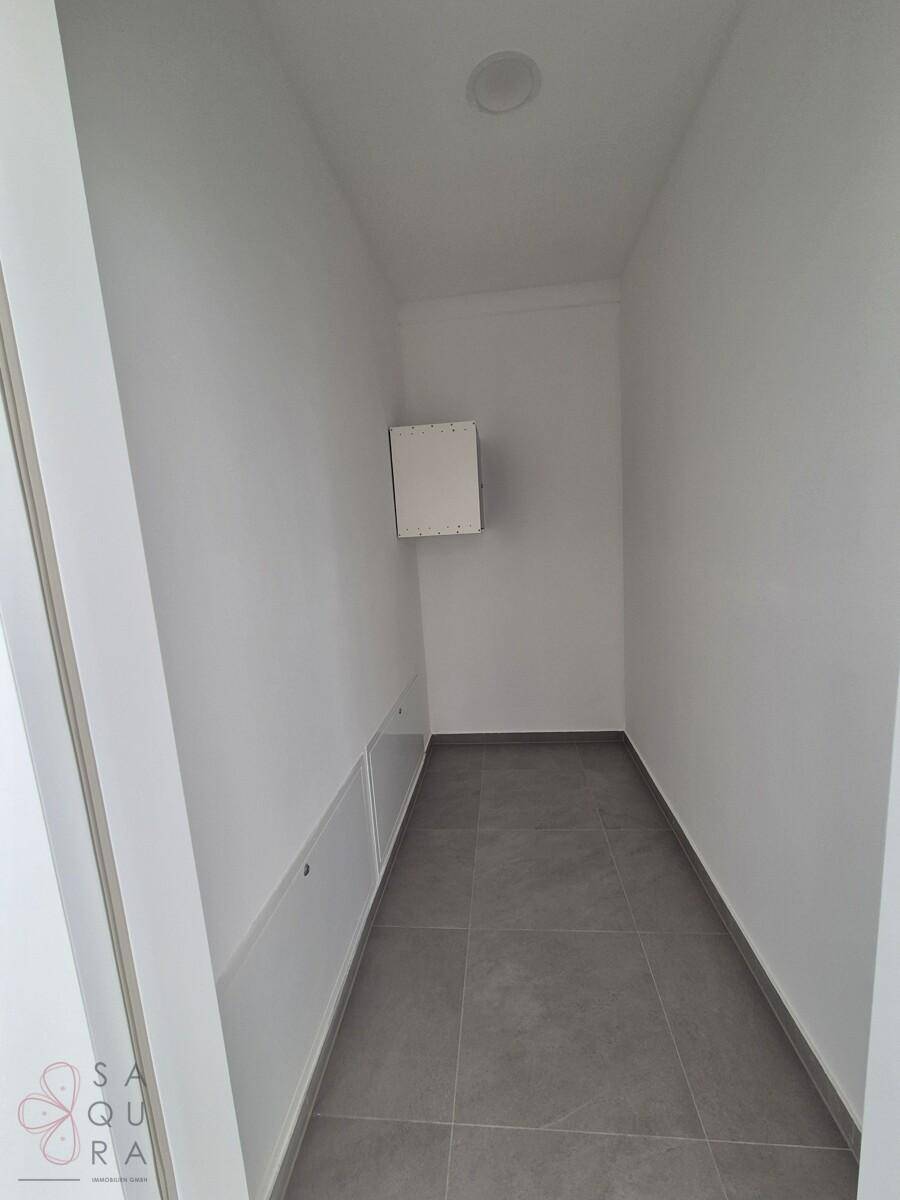 Schmaler Abstellraum mit weißen Wänden und grauen Fliesen, ideal für Lagerzwecke.