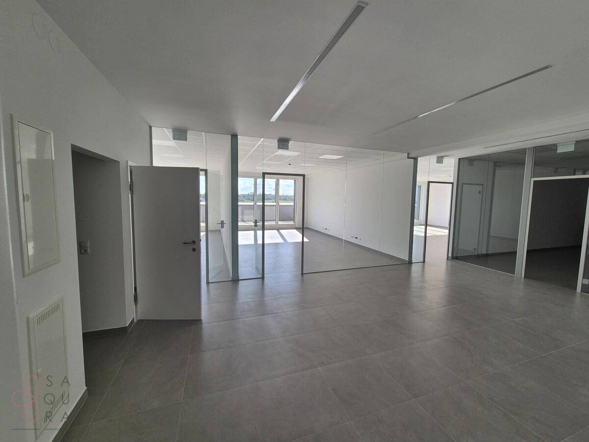 Geräumiger Bürobereich mit Glaswänden, die separate Arbeitsbereiche schaffen, und großen Fenstern.